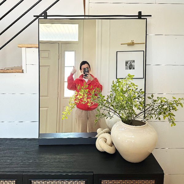 Rectangular wall mirror with black metal frame and reflective glass showing person