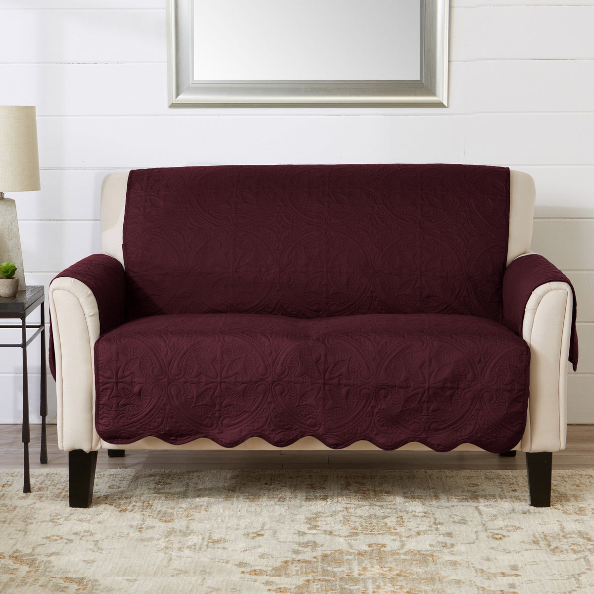 Wine red loveseat furniture protector with patterned quilted fabric and scalloped edge.