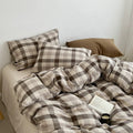 Brown-and-gray plaid duvet cover set with pillow shams and folded blankets on the bed.