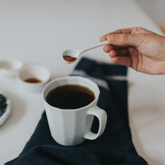Handmade porcelain coffee mug, matte white, held while pouring with a spoon