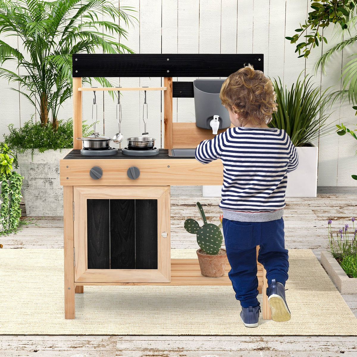 Kids outdoor play kitchen with black cooktop and gray sink; child reaching forward