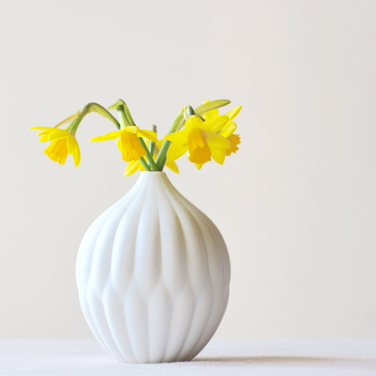 Small white porcelain vase with ribbed textured surface, topped with yellow flowers