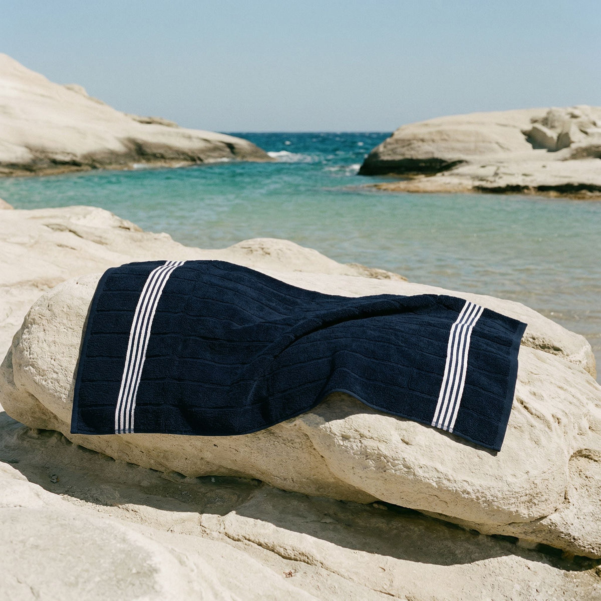 Rolled navy Australian cotton towel with white stripe bands on rock