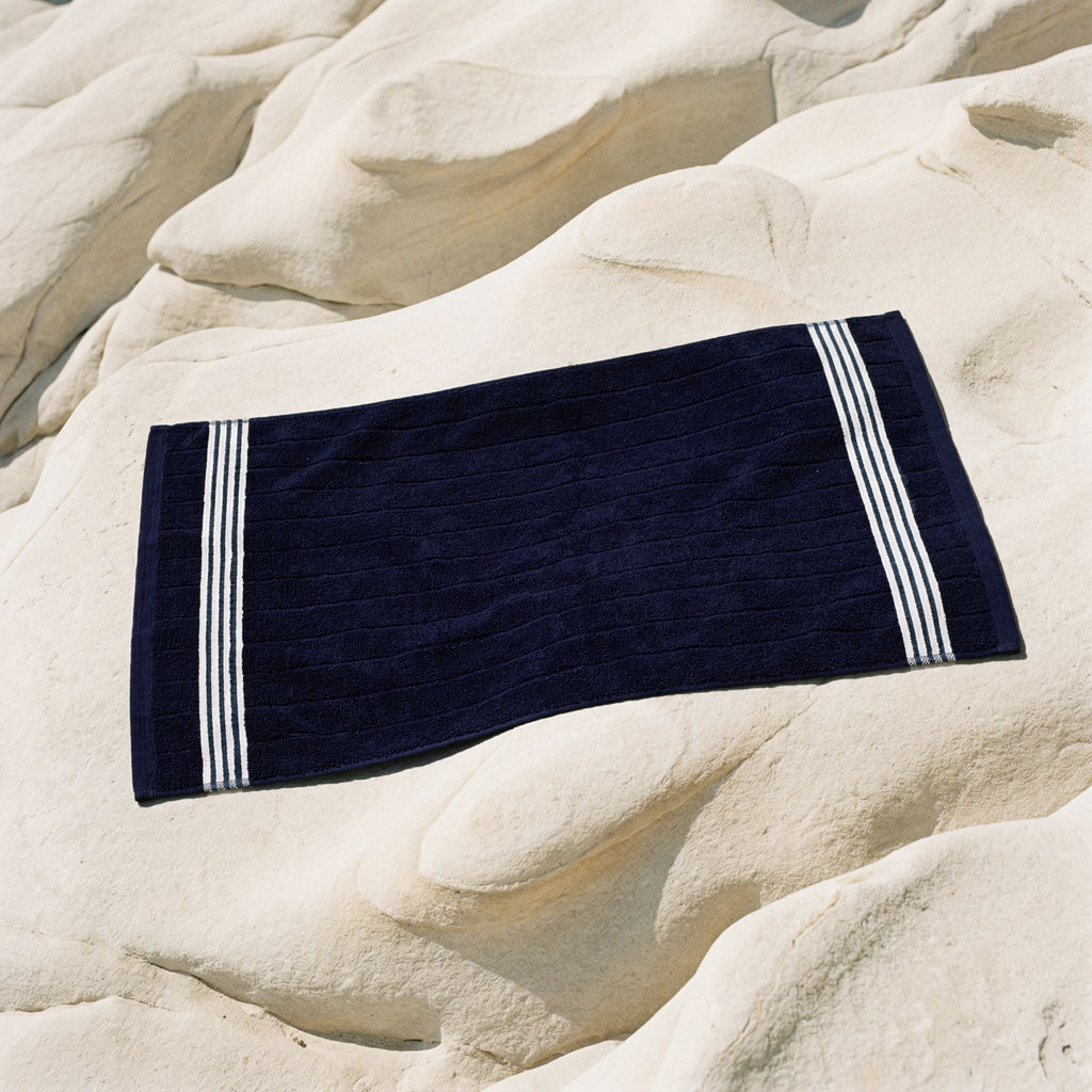 Navy Australian cotton towel with white striped border, folded on rocks