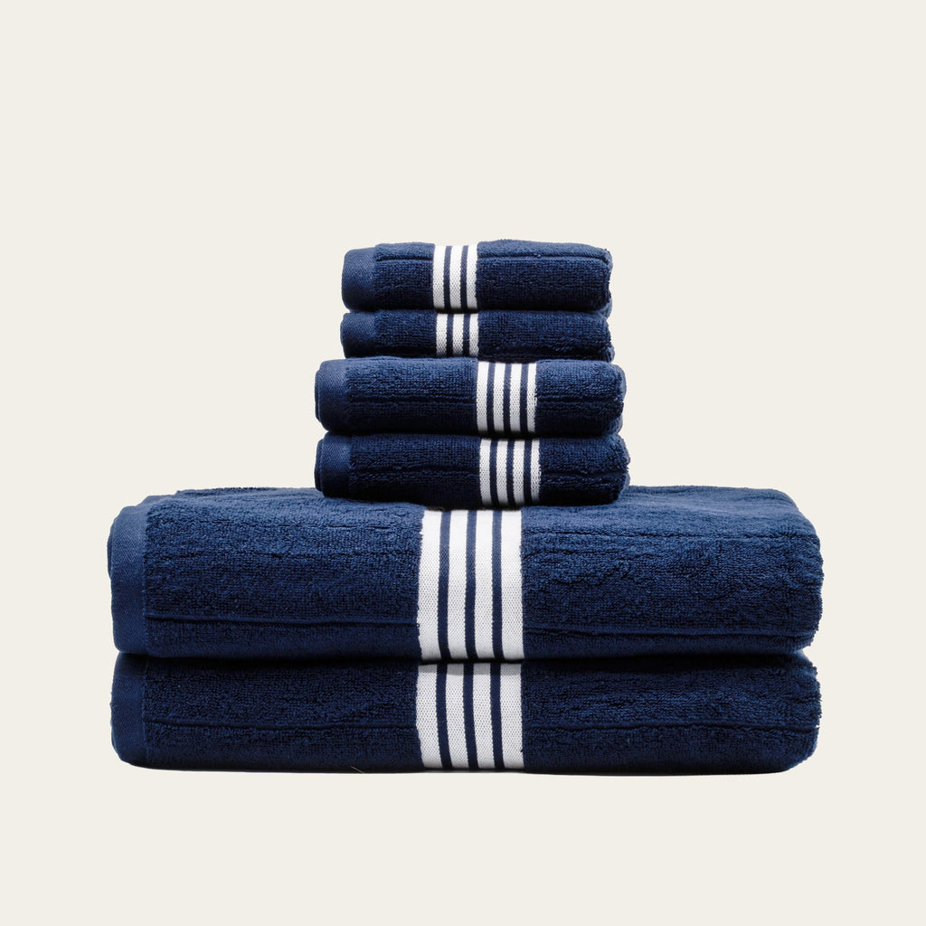Stacked navy cotton towels with white striped bands, folded into a multi-piece set