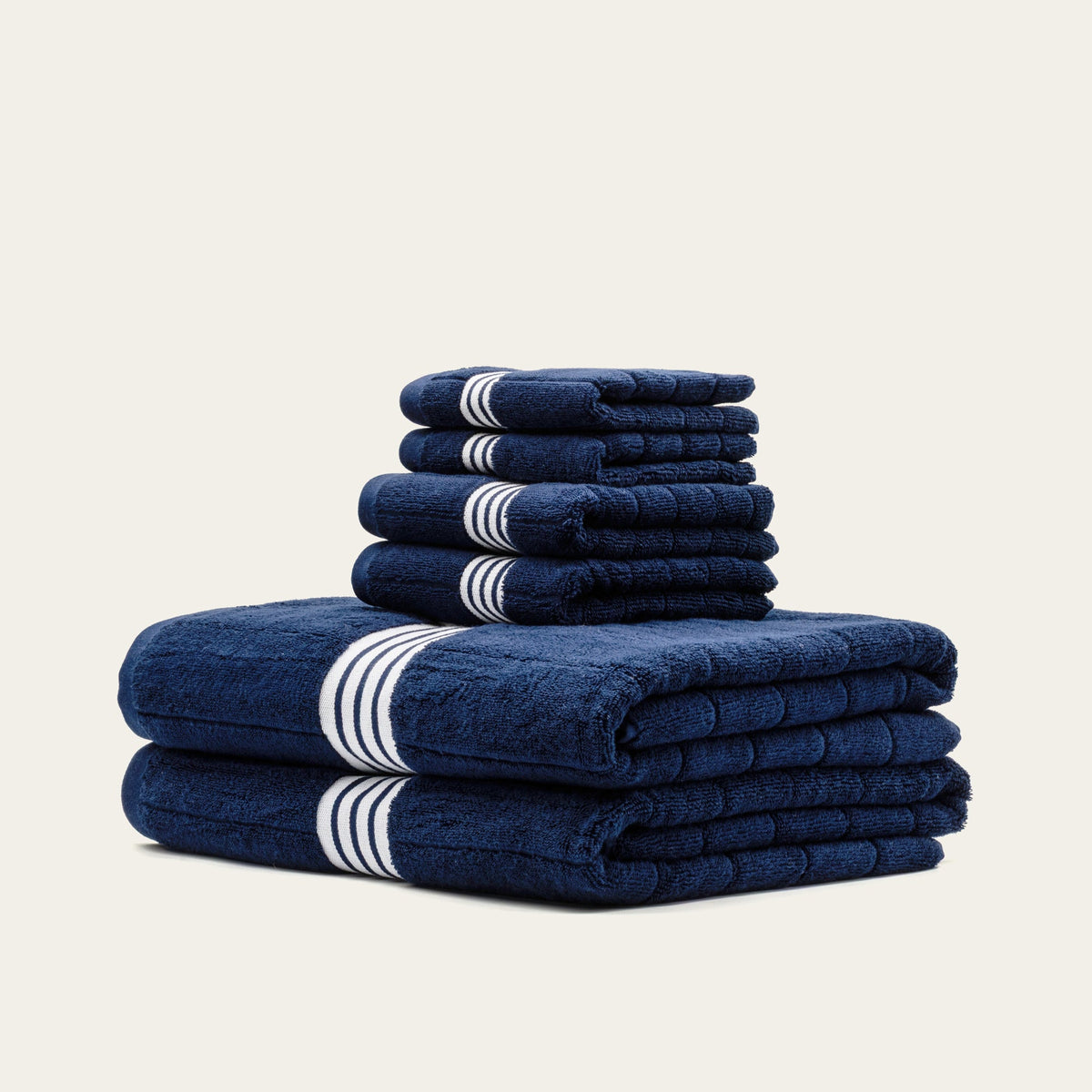 Tall stack of navy towels with white striped bands, folded into a set