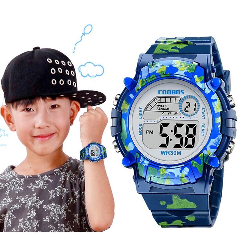 Kids blue digital camo LED wristwatch with round LCD display, WR30M, on wrist.