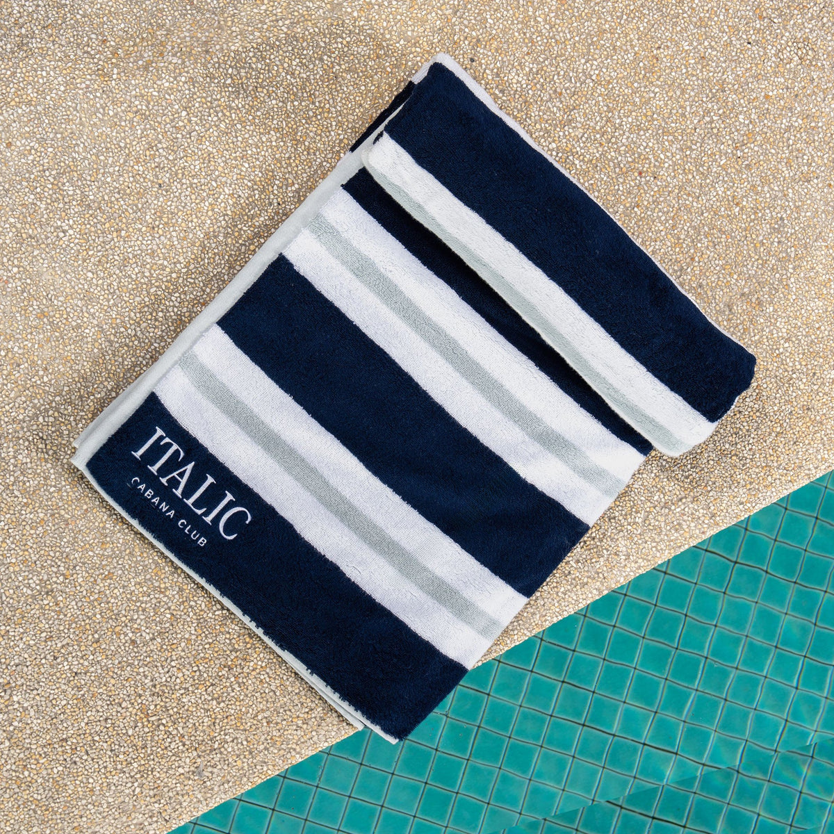 Cotton beach towel with navy and white striped pattern on sand, branded “ITALIC”