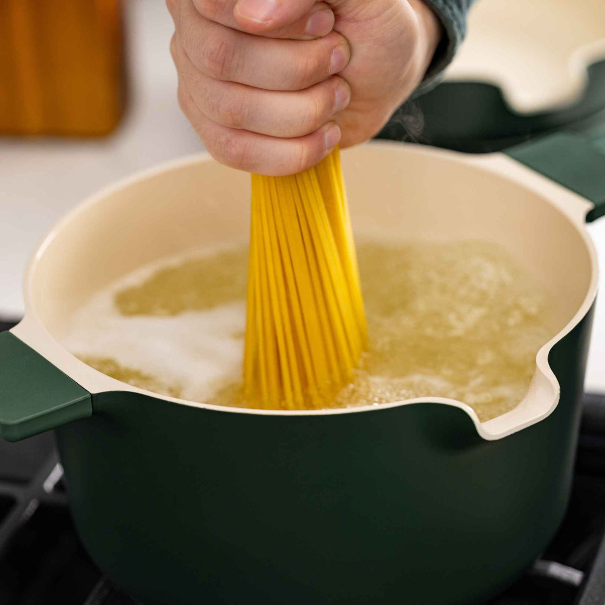Green ceramic nonstick pot pouring spaghetti strands into the pan