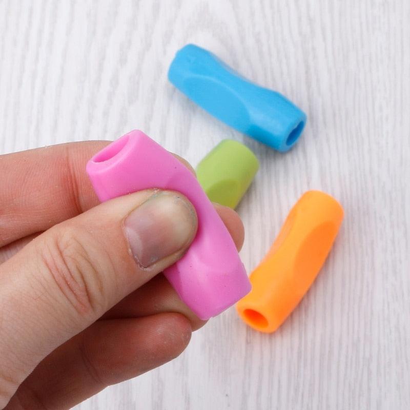 Hand holding pink pencil grip on black pen; blue, green, and orange grips nearby