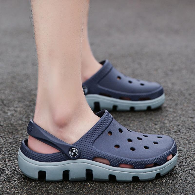 Navy slip-on clogs with perforations and adjustable back strap on an outdoor pavement