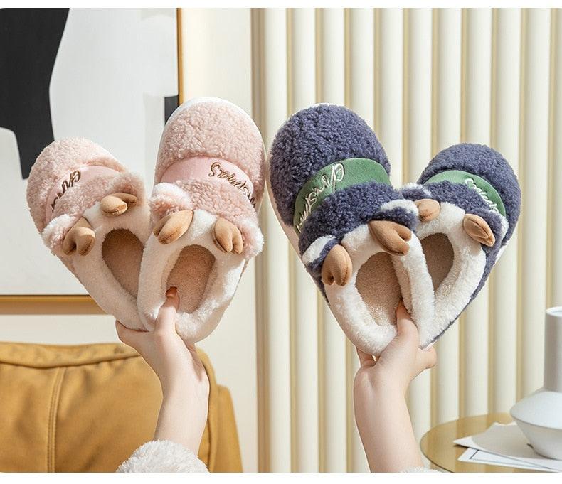 Plush deer Christmas slippers held up: pink and dark gray pairs with antler tops.