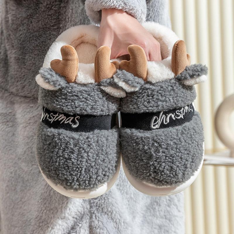 Gray plush deer slippers with black band, antler appliques, and “Christmas” script