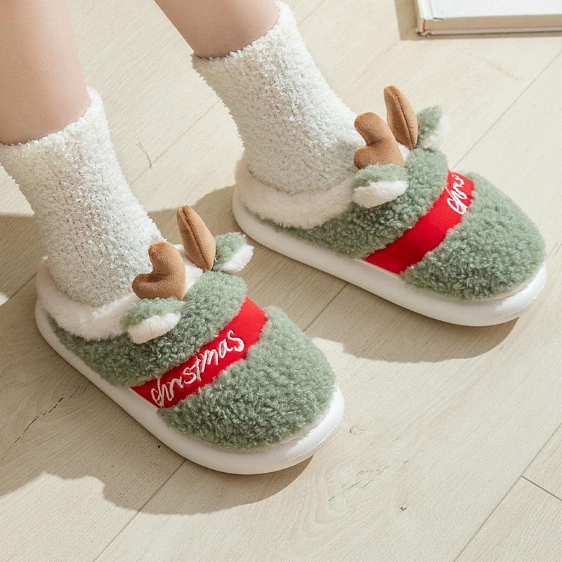 Green plush deer Christmas slippers with red belt trim and antler appliques.