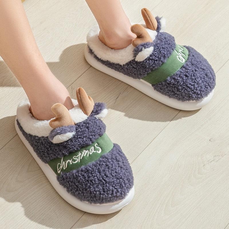 Purple plush deer Christmas slippers with antler details and green belt trim.
