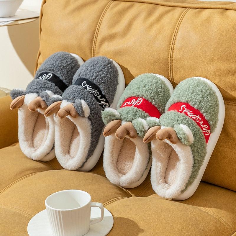 Assorted plush deer Christmas slippers on sofa, green, gray, cream, and red pairs.