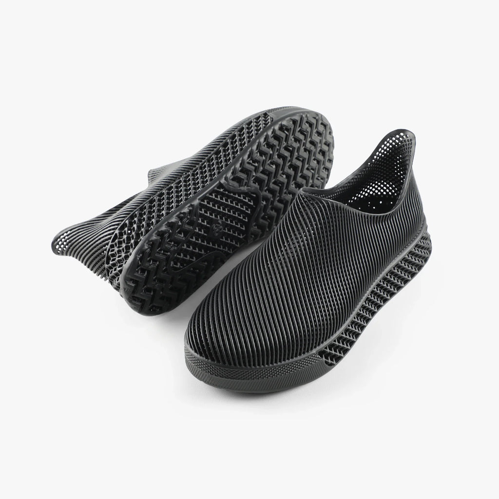 Black 3D printed slip-on sneakers shown with treaded outsole and ribbed upper