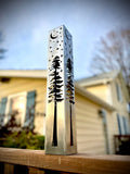 Silver steel solar light pillar on a wooden step with moon, stars, and pine tree cutouts.