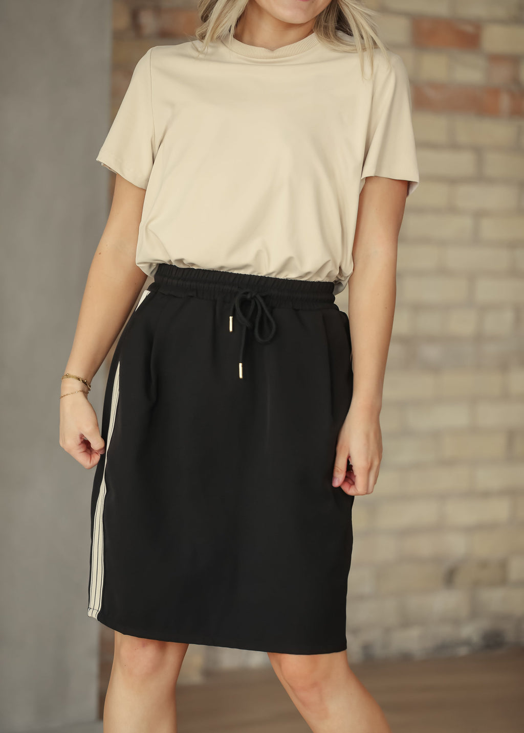 Black mid-rise track skirt with white side stripes and drawstring waist, knee length