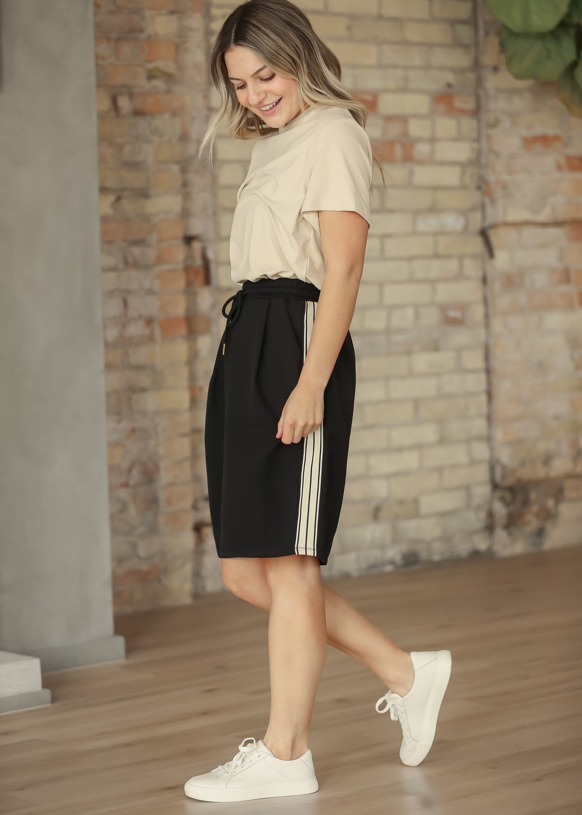 Black mid-rise track skirt with white side stripes and gathered drawstring waist