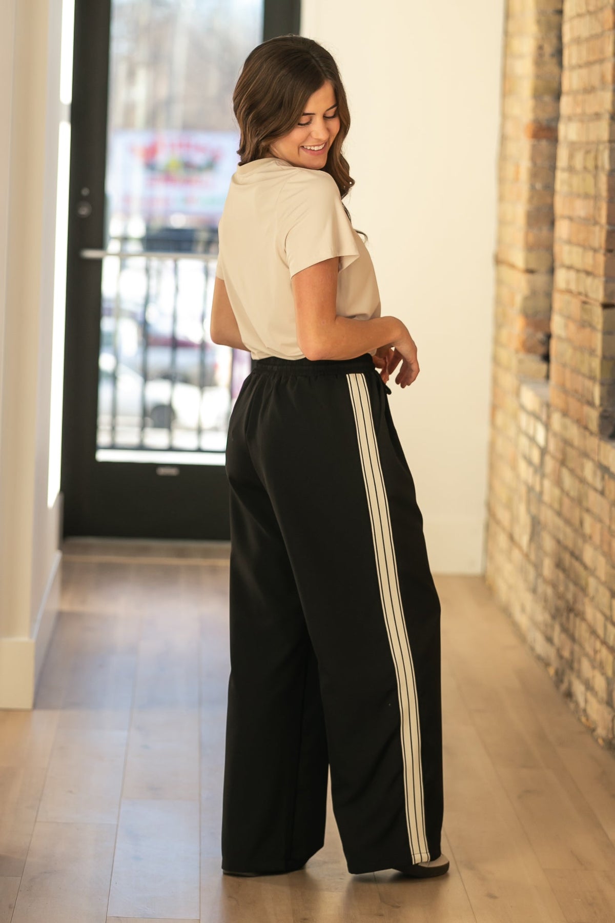 Black wide-leg track pants in profile with white side stripes and drawstring