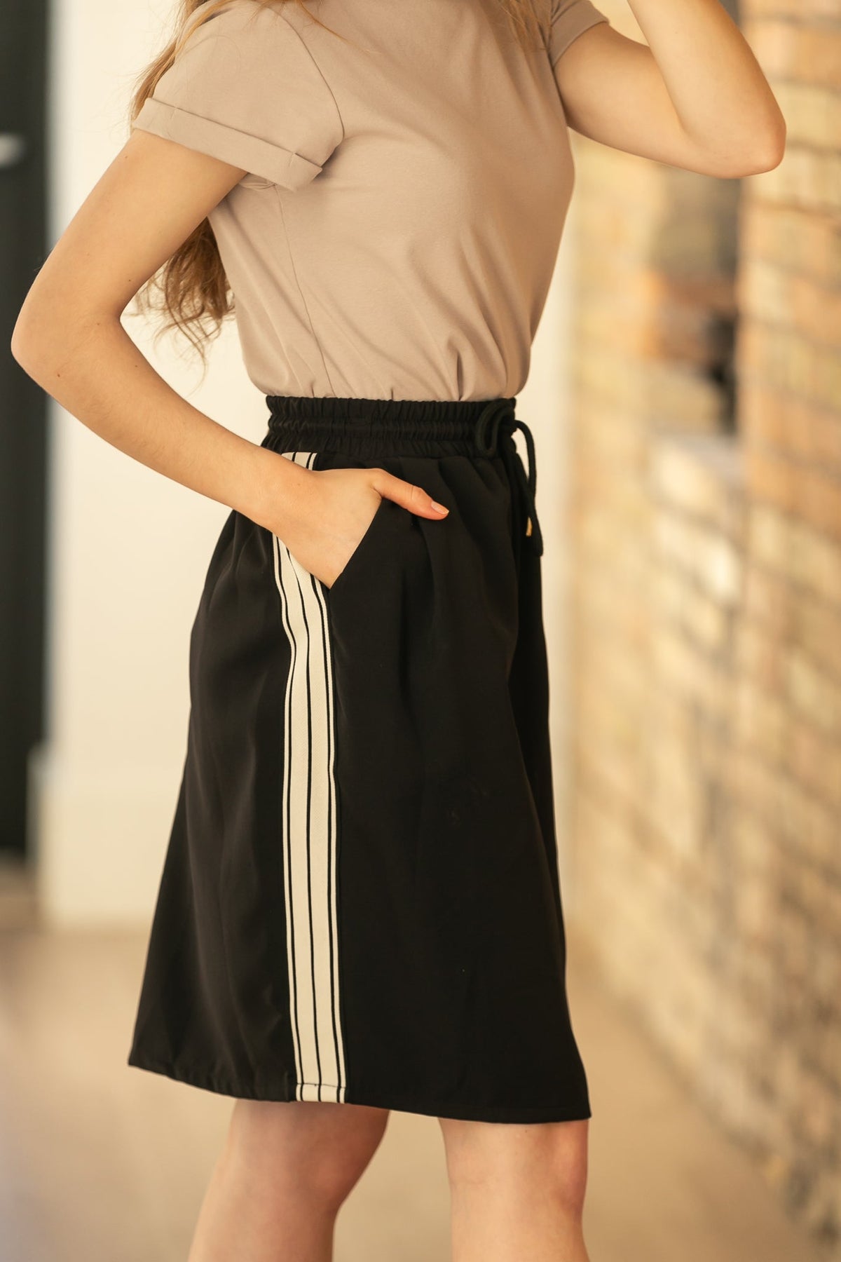 Black mid-rise track skirt with side stripe panel detail and drawstring elastic waist.