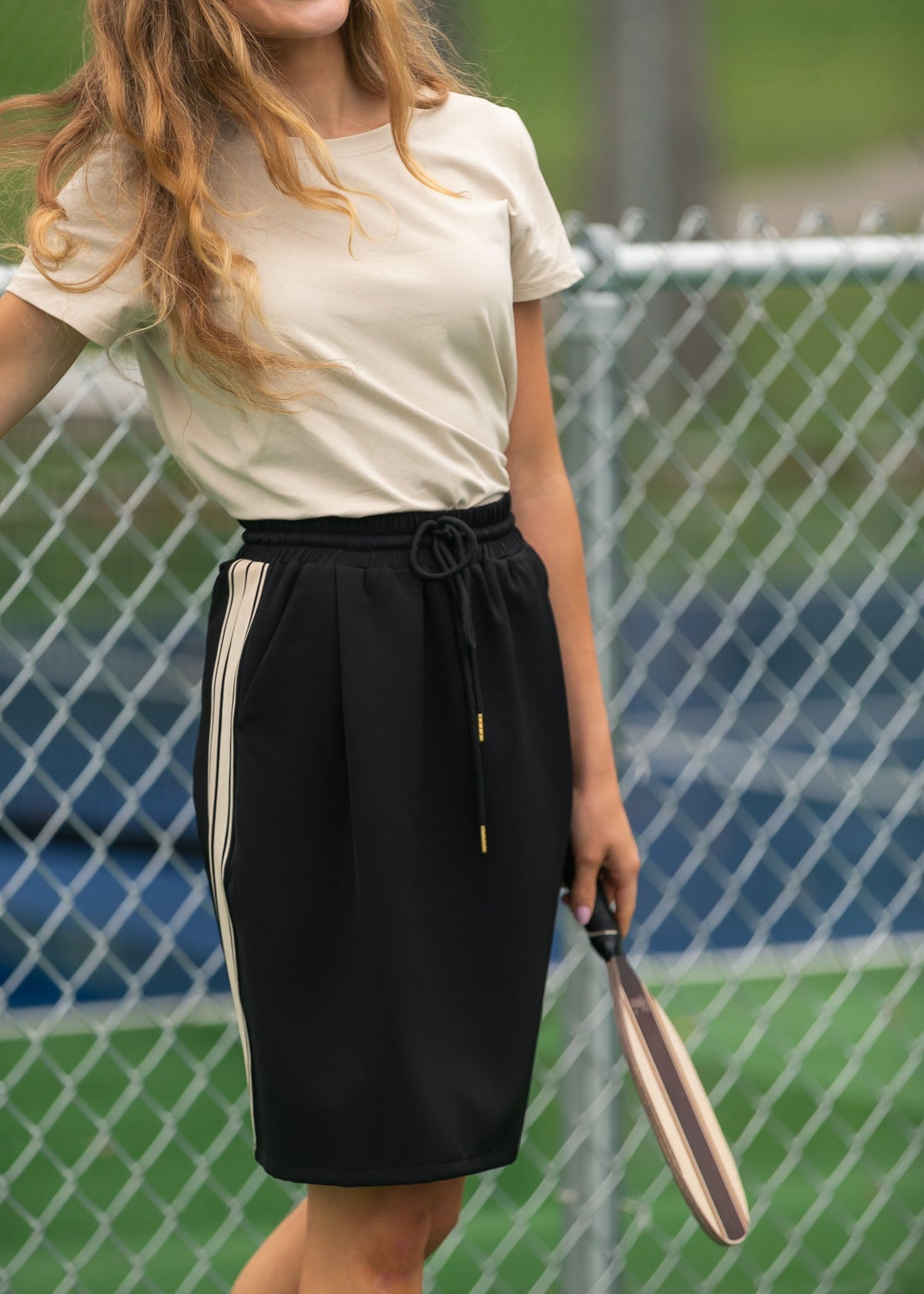 Black mid-rise track skirt, knee-length, with drawstring waist and white side stripe
