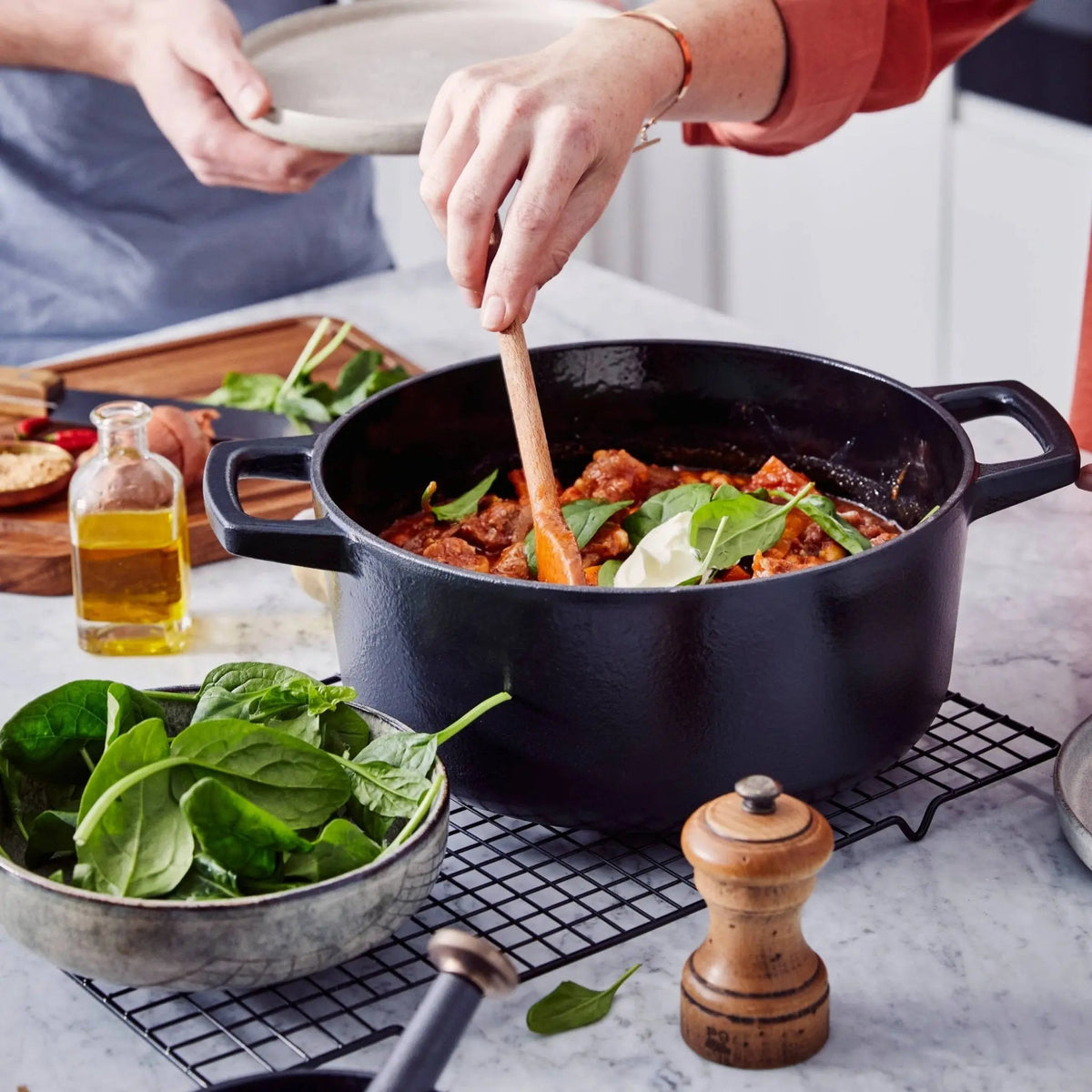 Dark navy enameled cast iron Dutch oven with two handles, filled with cooked food.