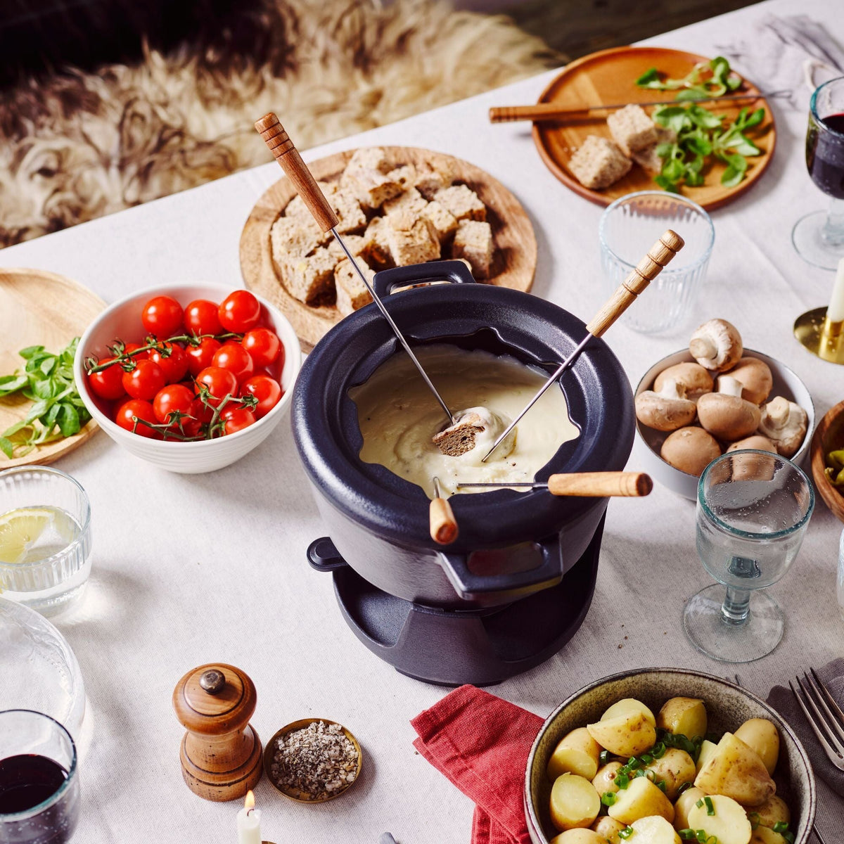 Black fondue pot with burner base and wooden forks resting on top