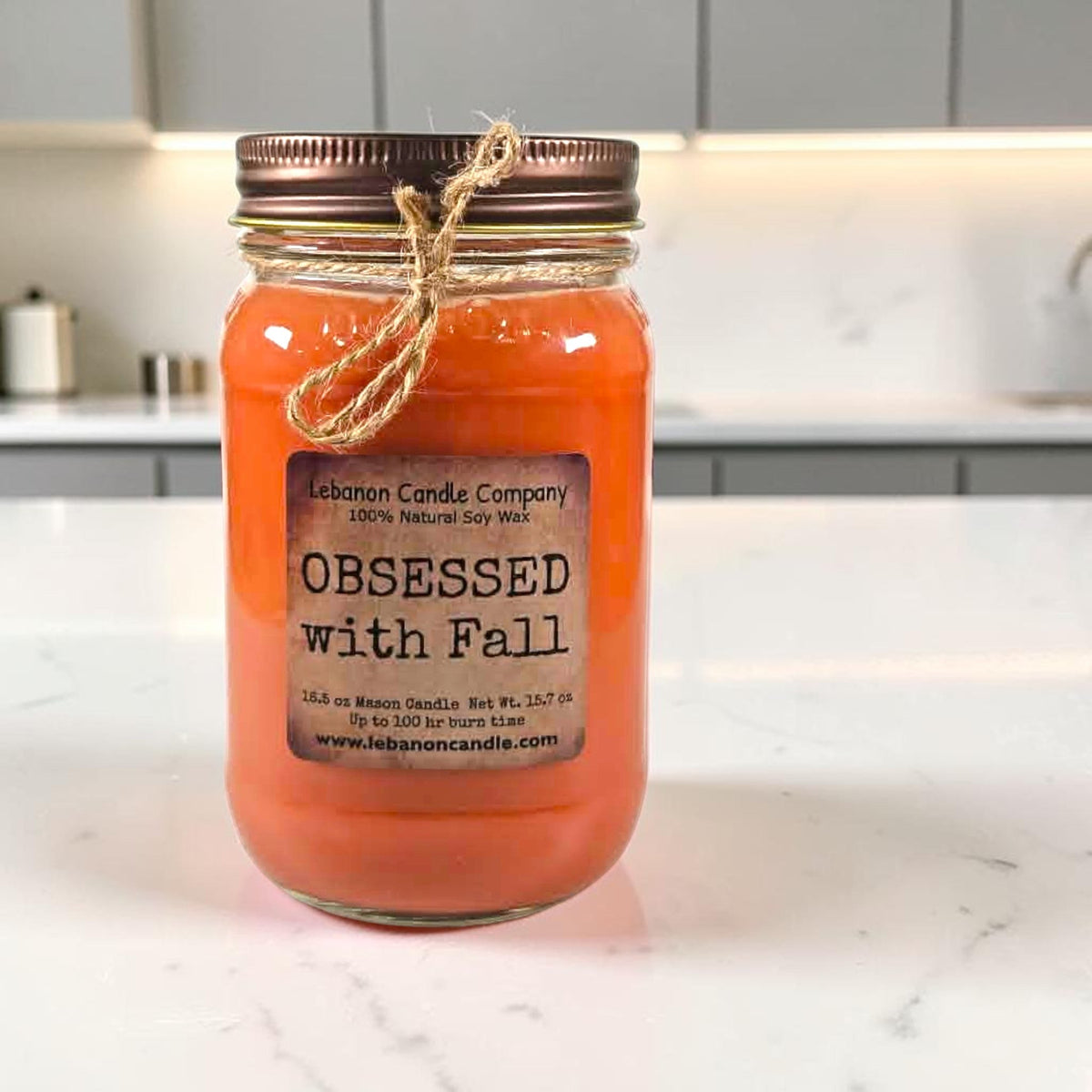 Orange jar candle in glass jar with twine bow and centered label