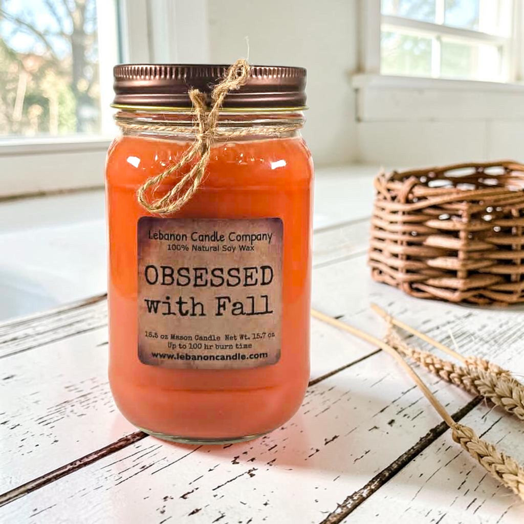 Orange jar candle with twine bow and printed label on whitewashed wood
