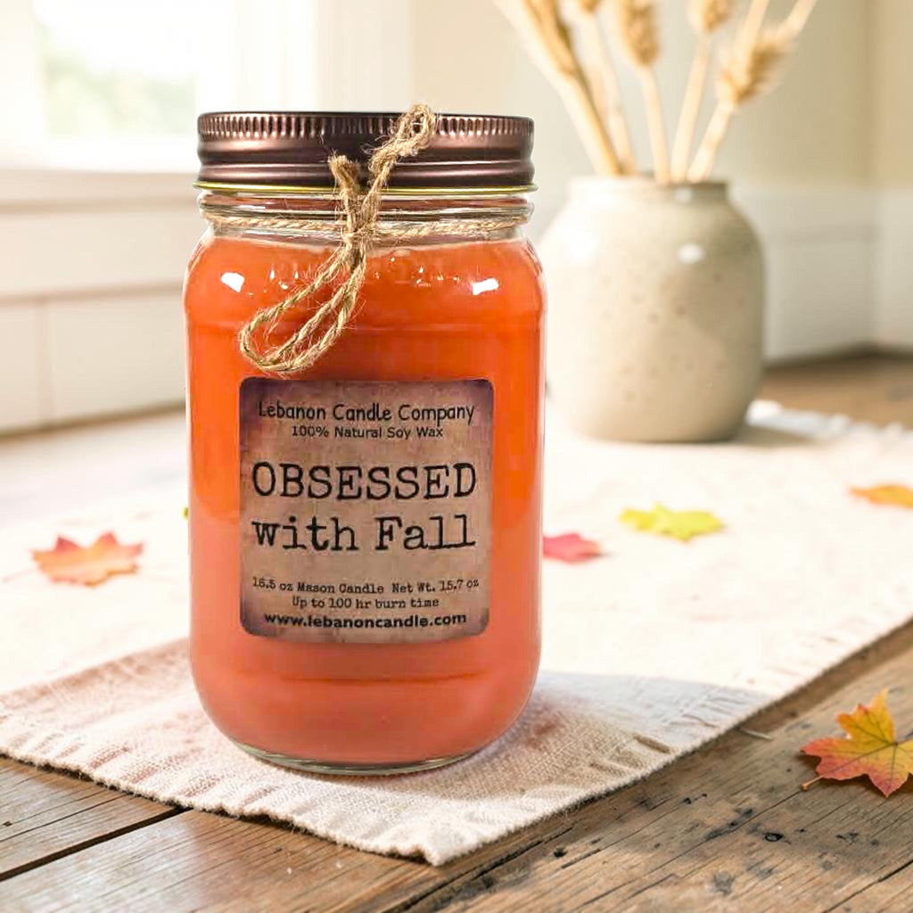 Orange jar candle with twine tied bow on tabletop with fall leaves nearby