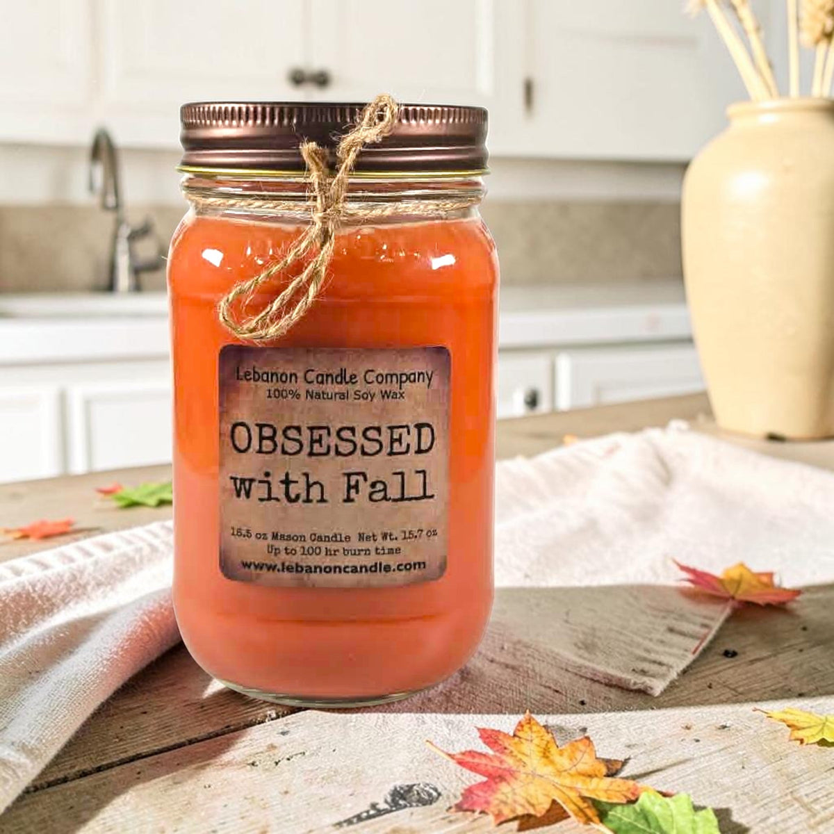 Orange jar candle with twine bow and printed label on wooden tabletop