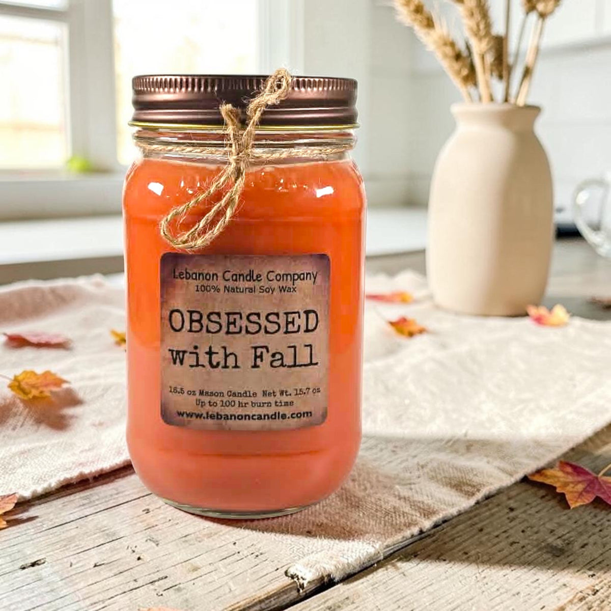 Orange jar candle with twine bow, printed label front, and no lid flame