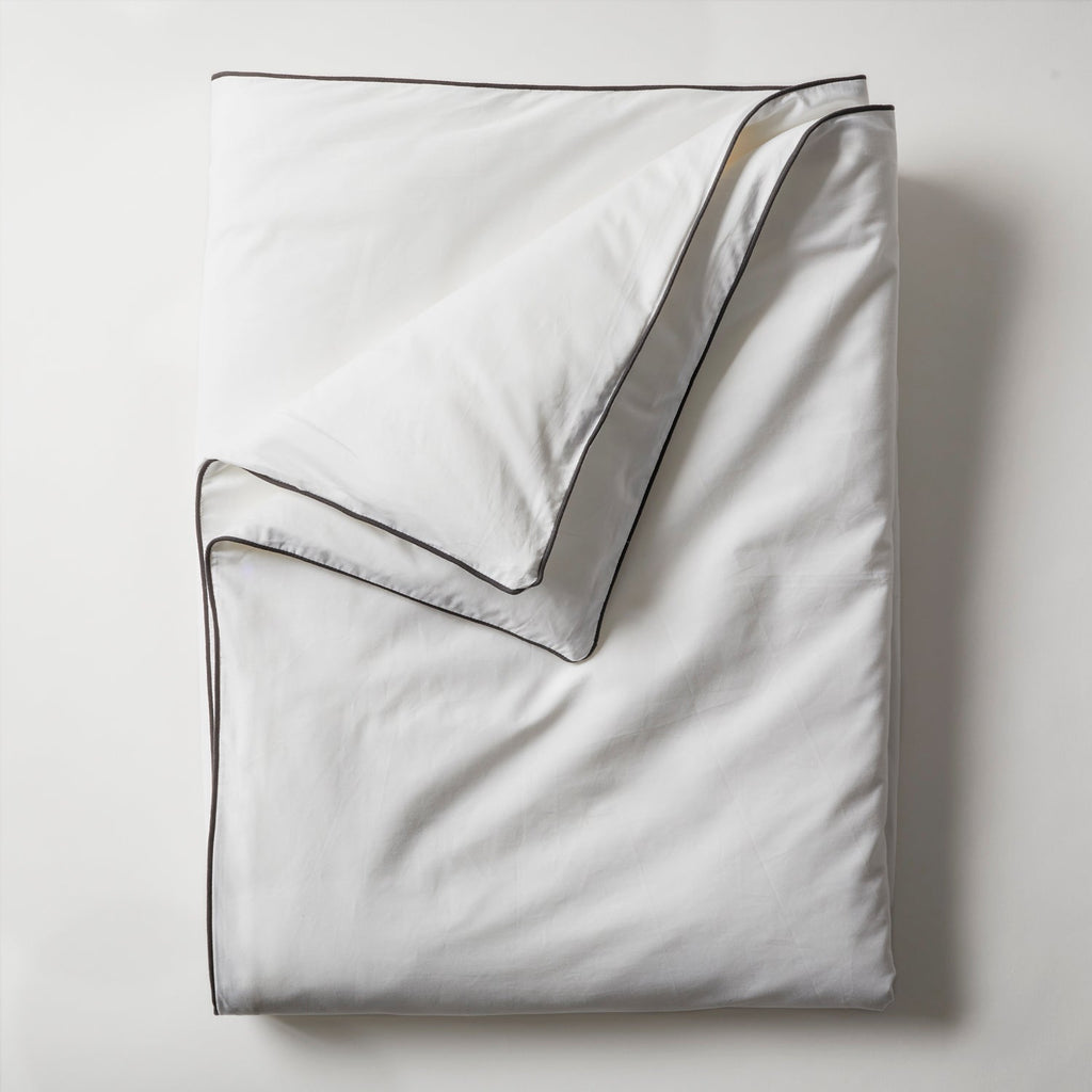 White silk throw with dark piping, folded flat.