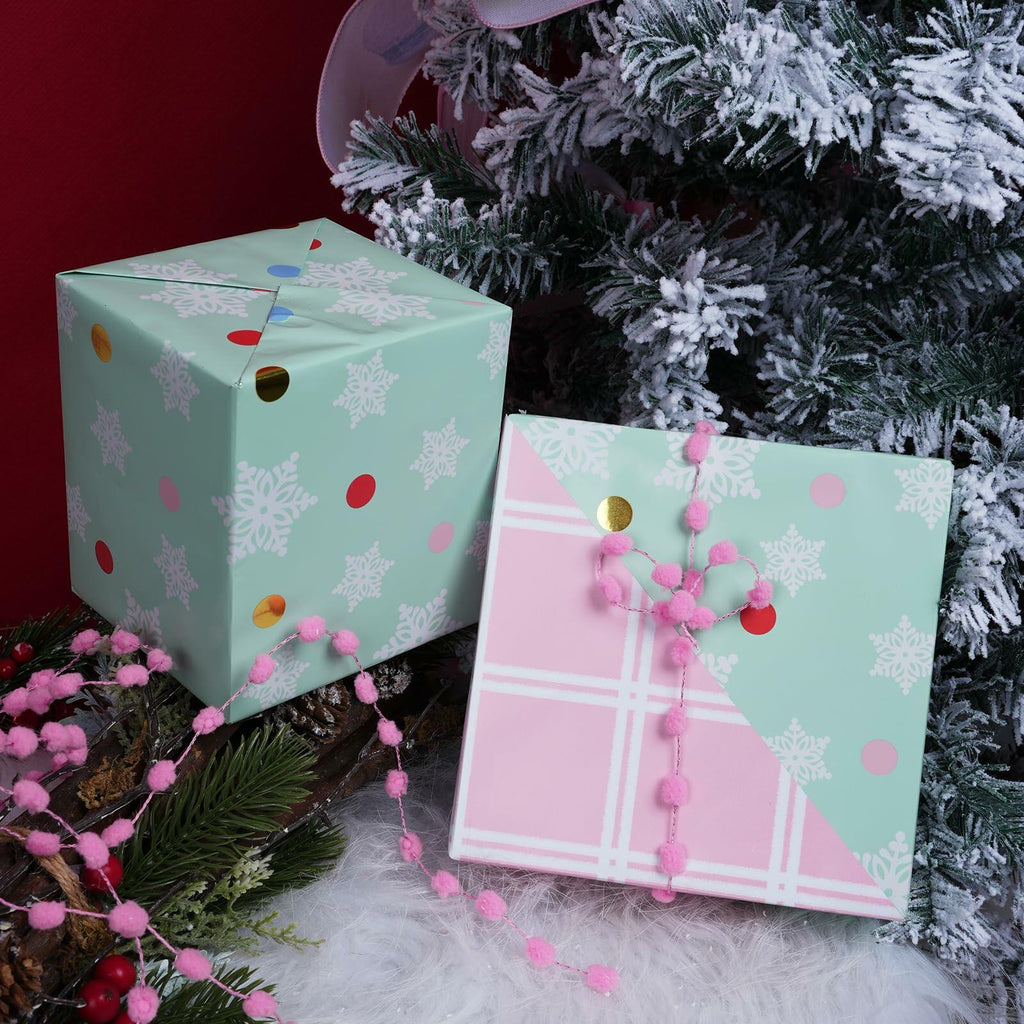 Christmas gift wrap boxes with mint snowflake and pink plaid designs, tied with pink pom garland