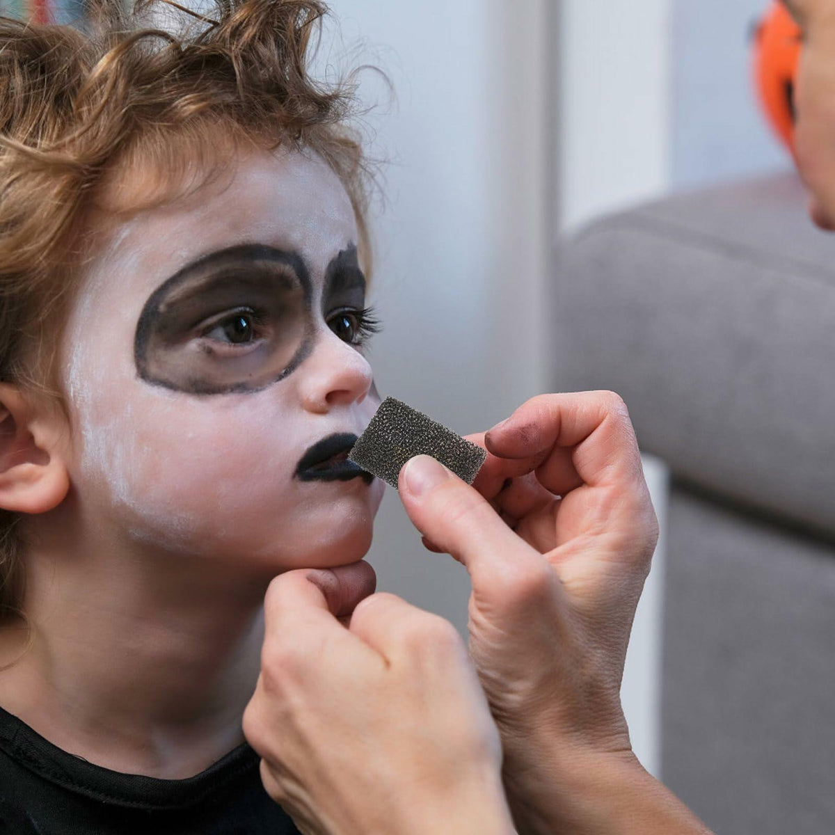 Black foam sponge held to apply costume makeup on a child’s face