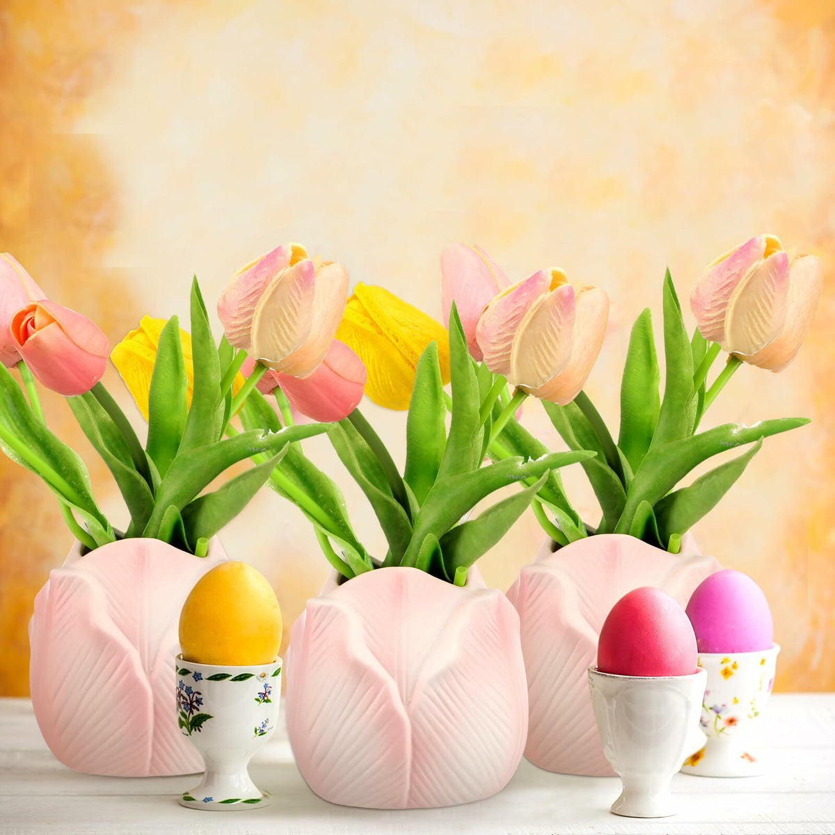 Pink tulip-shaped ceramic mini vases holding tulip-style flowers on a table