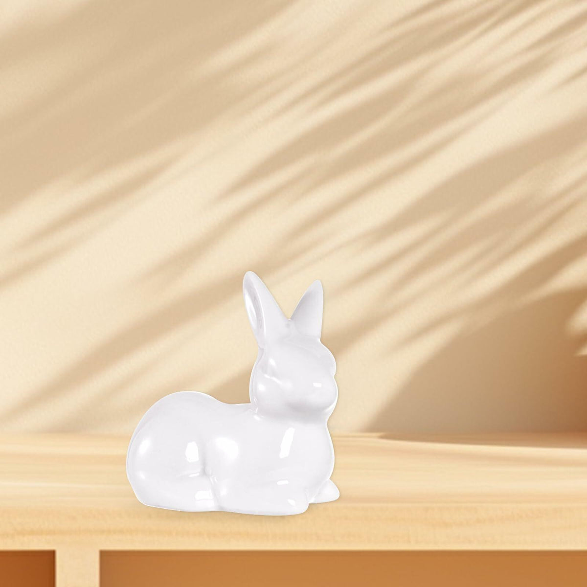 White ceramic Easter bunny figurine on wooden ledge, small glossy seated rabbit with upright ears.