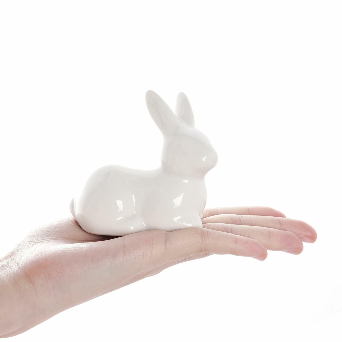 White ceramic Easter bunny figurine held in hand, glossy seated rabbit with upright ears.