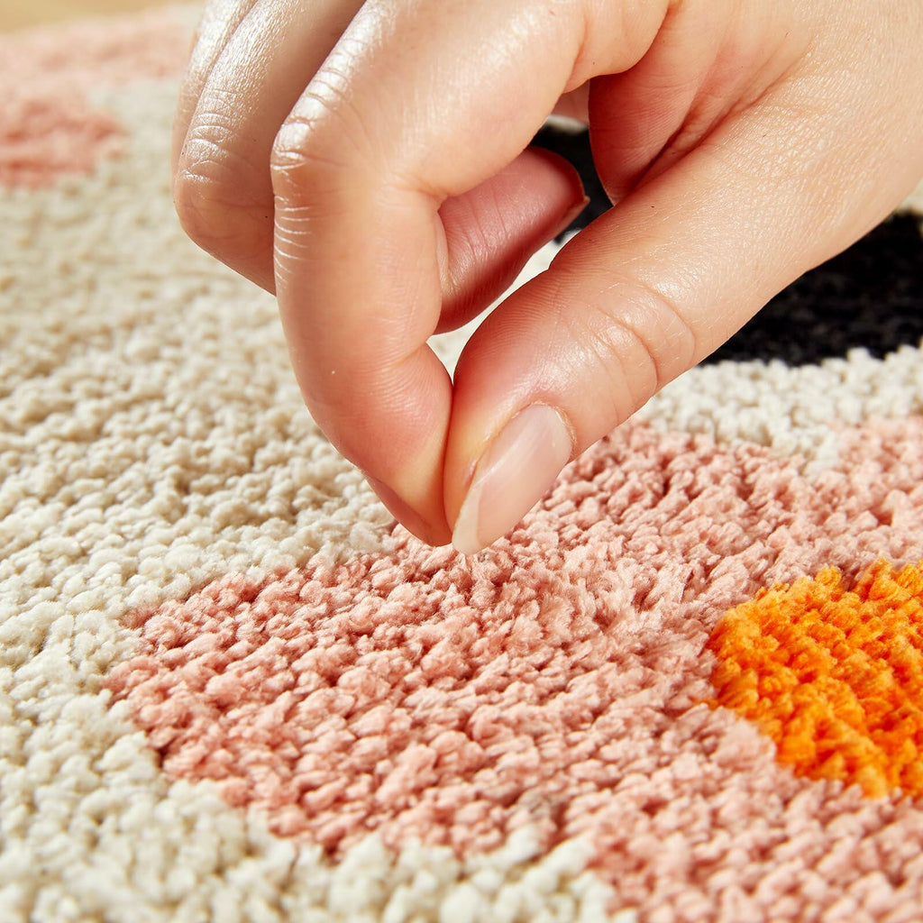 Hand pressing a plush beige bath mat with orange and pink flower details
