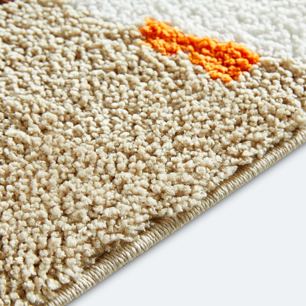 Corner close-up of beige bath mat with textured loop pile and orange accent