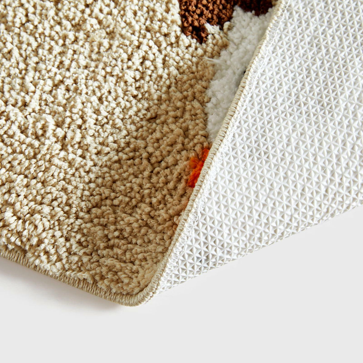 Beige bath mat edge showing textured surface and white non-slip backing