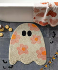 Beige ghost-shaped bath mat with black eyes and orange-pink floral pattern