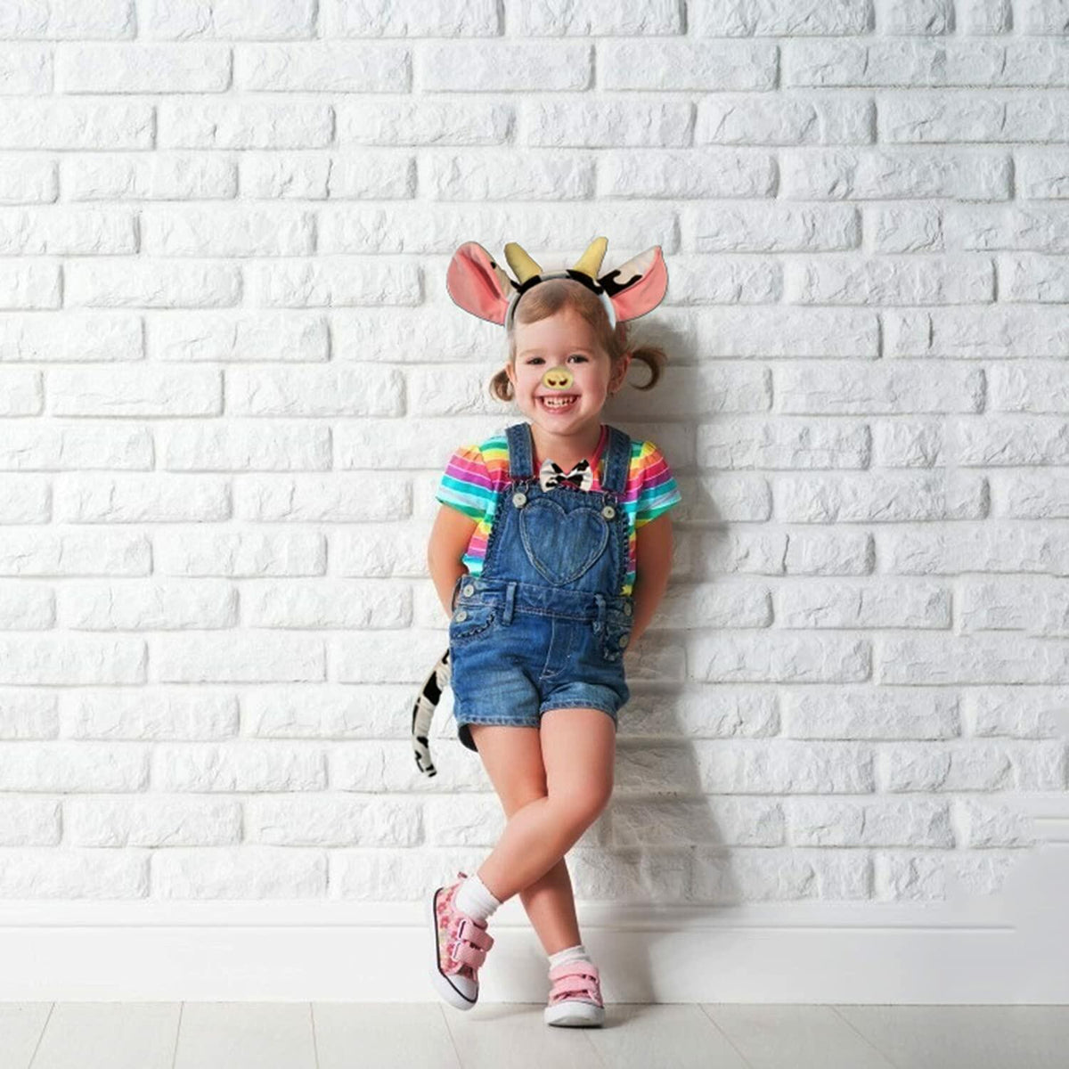 Child wearing cow ears headband costume set in black, white, and pink plush