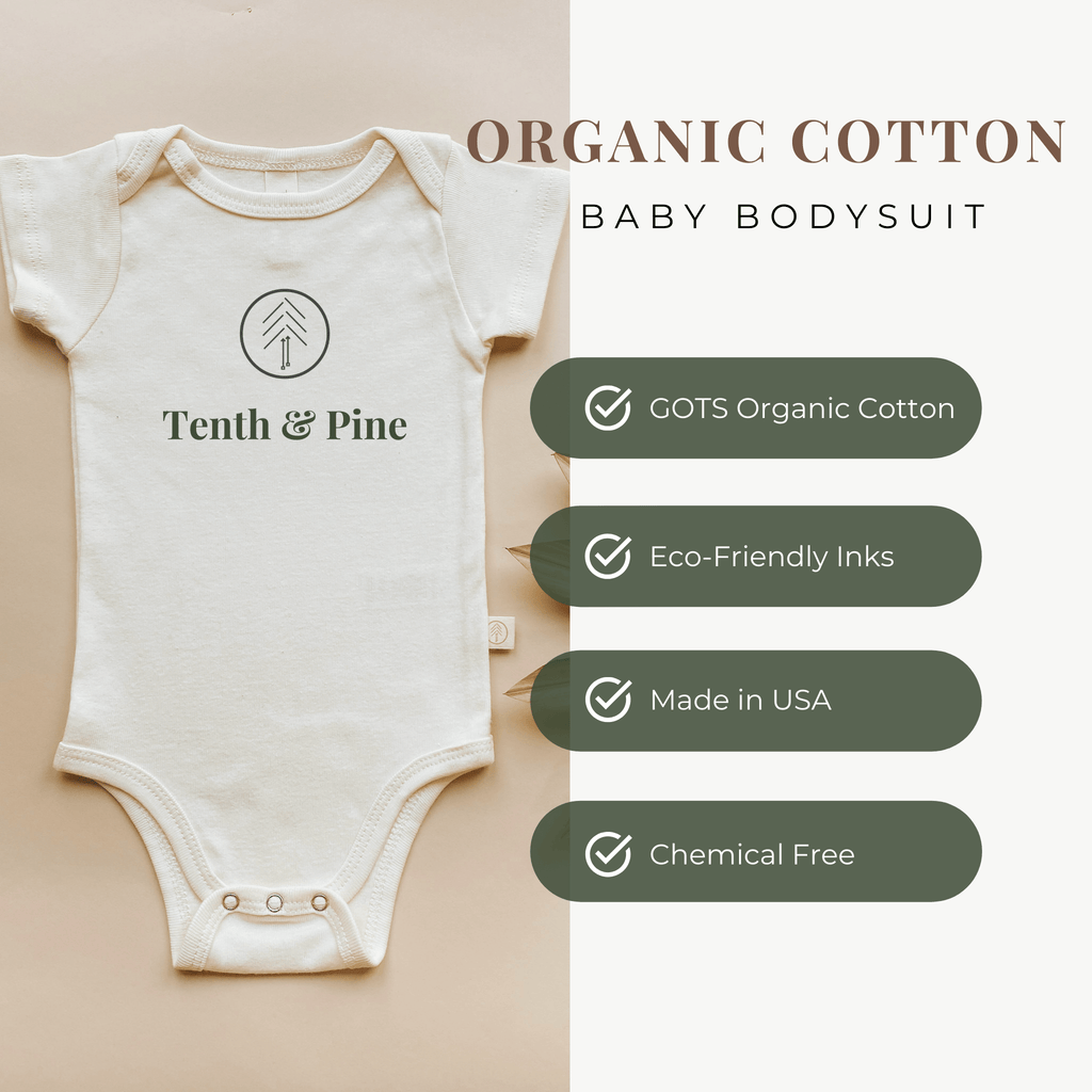 Cream Tenth & Pine baby bodysuit with tree/figures logo graphic on front.