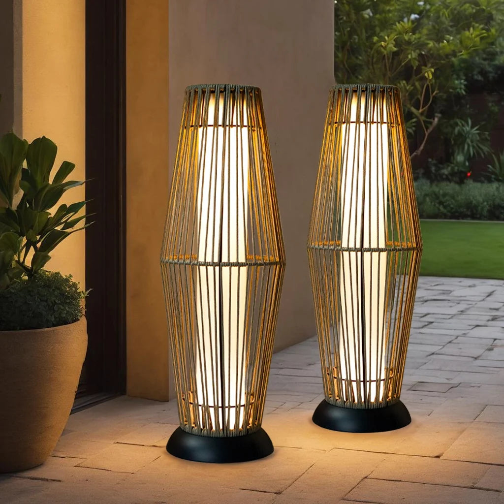 Pair of outdoor solar wicker lantern floor lamps with glowing glass cylinder and black bases