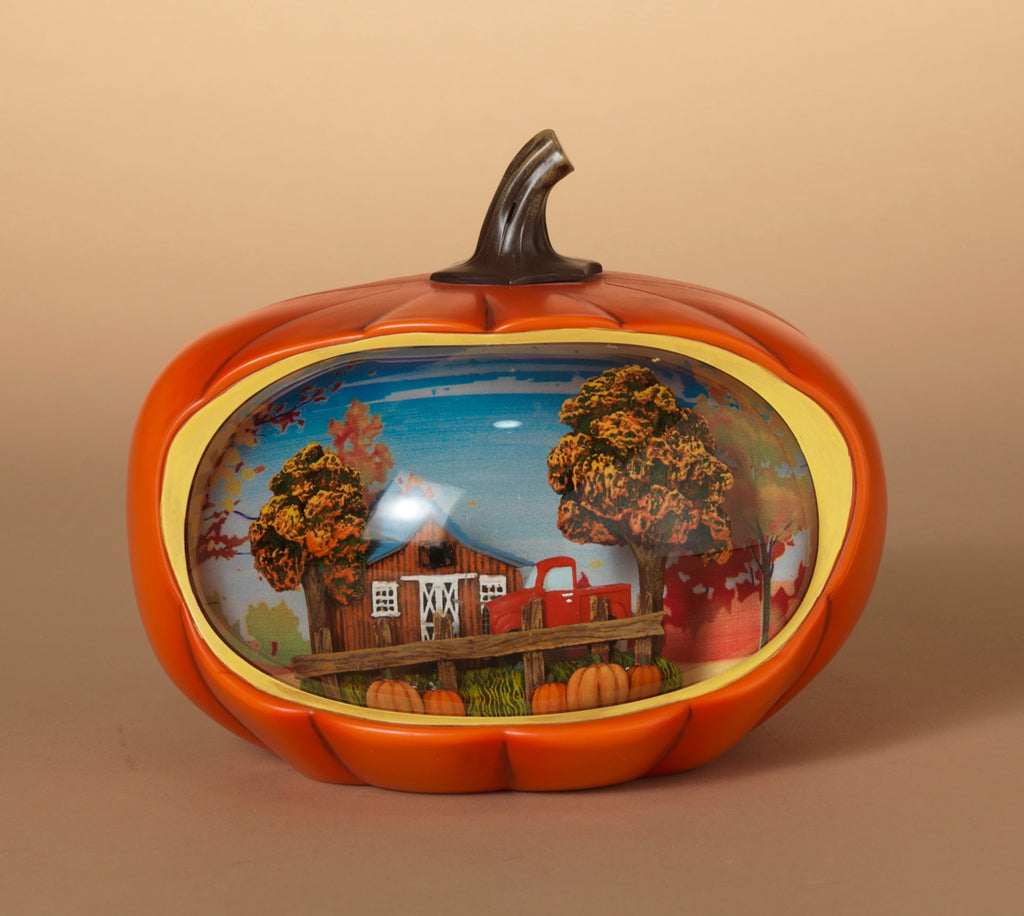 Orange pumpkin-shaped lighted water globe with trees and house scene behind clear globe