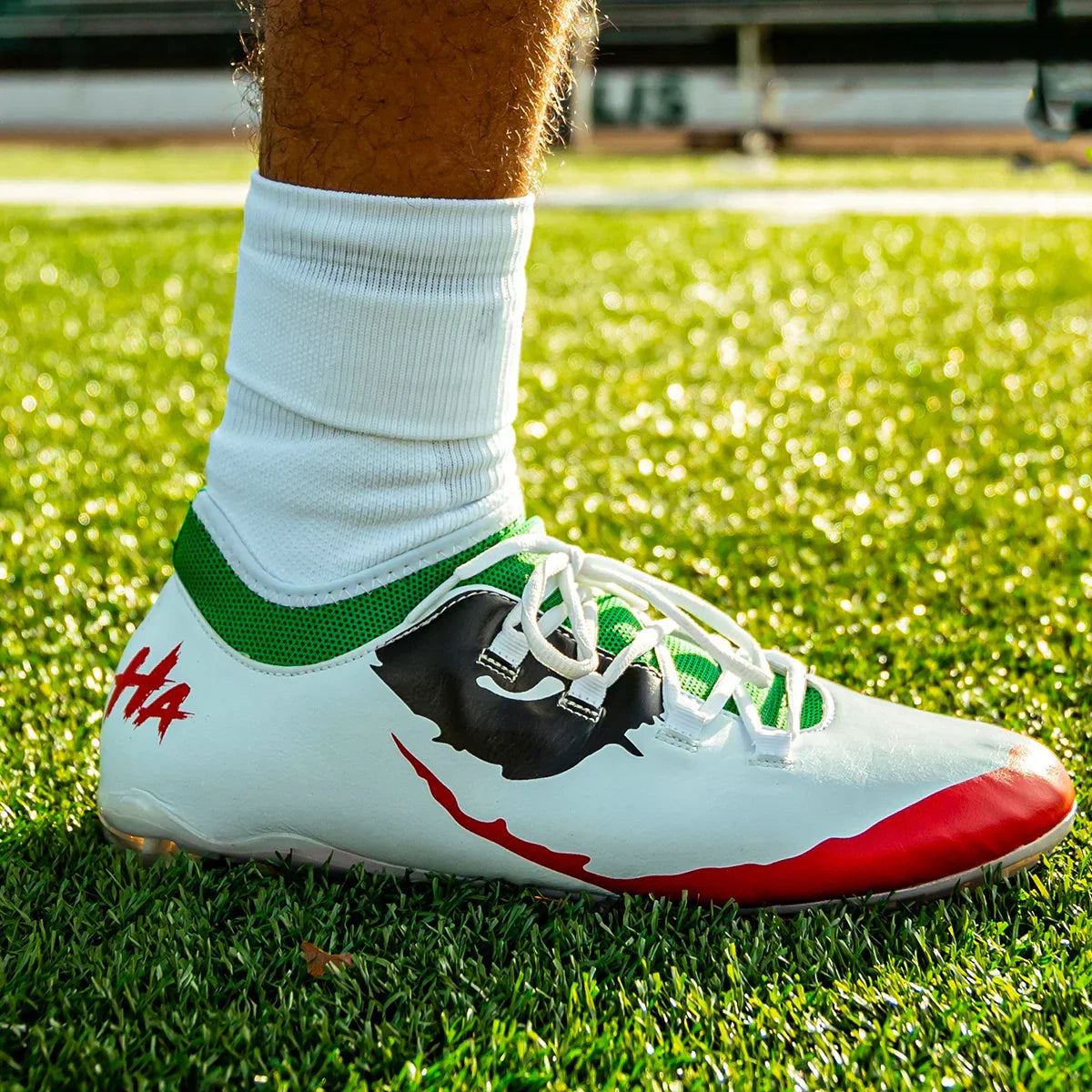 White soccer cleat with green accents and red sole on green outdoor grass