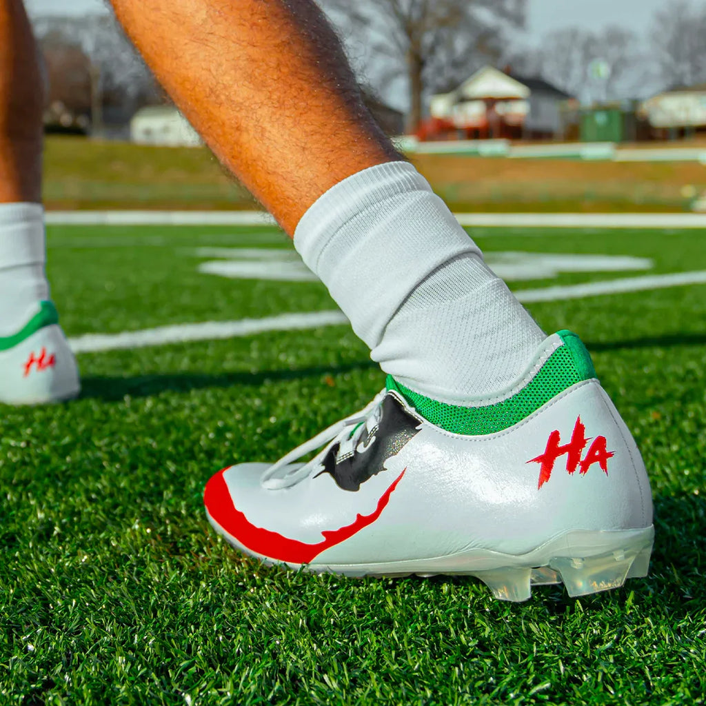 White-and-green soccer cleat with red logo on a field, worn with white sock